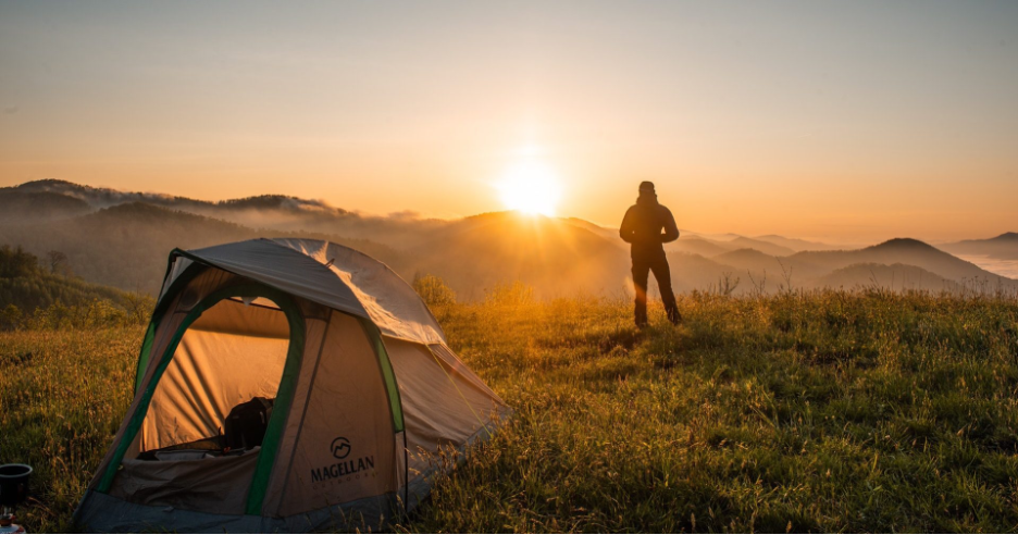 hiker in the mountains during sunset or sunrise with a pup tent in the foreground and mountain range in the backdrop illustrating skin and eye health in the mountains