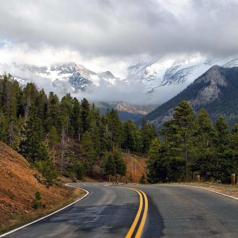 Winding mountain highway with evergreen trees and steep snow-covered mountains in the background