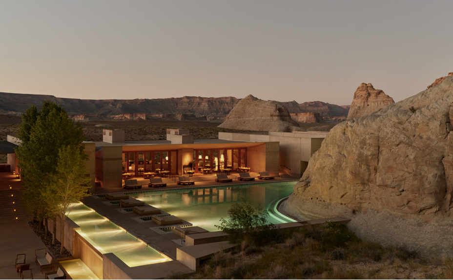 Bird's-eye view of the iconic Amangiri Resort – Canyon Point, Utah, with swimming pool wrapping around desert mountains, and interior public spaces glowing in the twilight